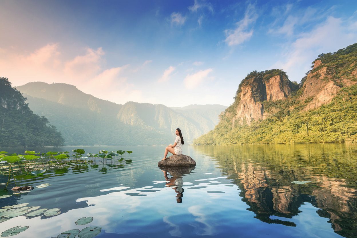 A young woman peacefully sitting on a rock in the middle of a lake
